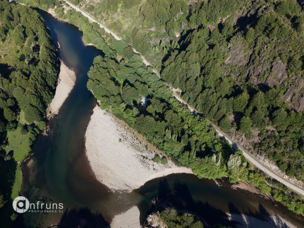 Top-down aerial view of a river bend with a gravel beach, dense forest, and a nearby road.