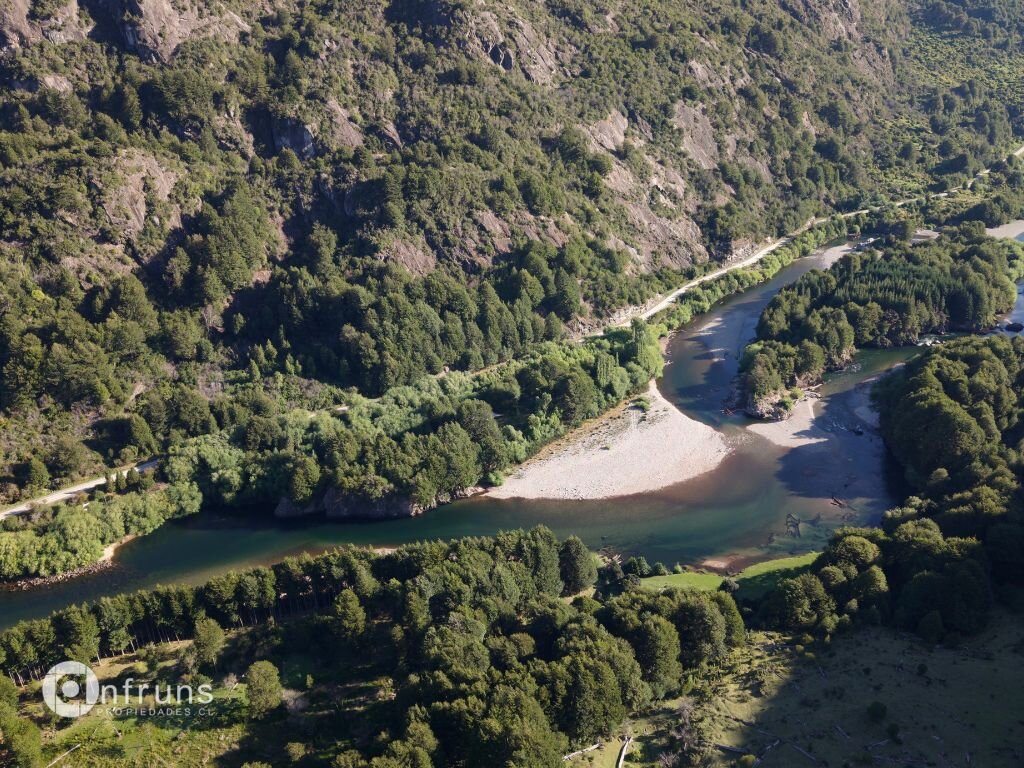 Aerial perspective of a scenic river bend surrounded by lush green forests and steep mountain slopes.