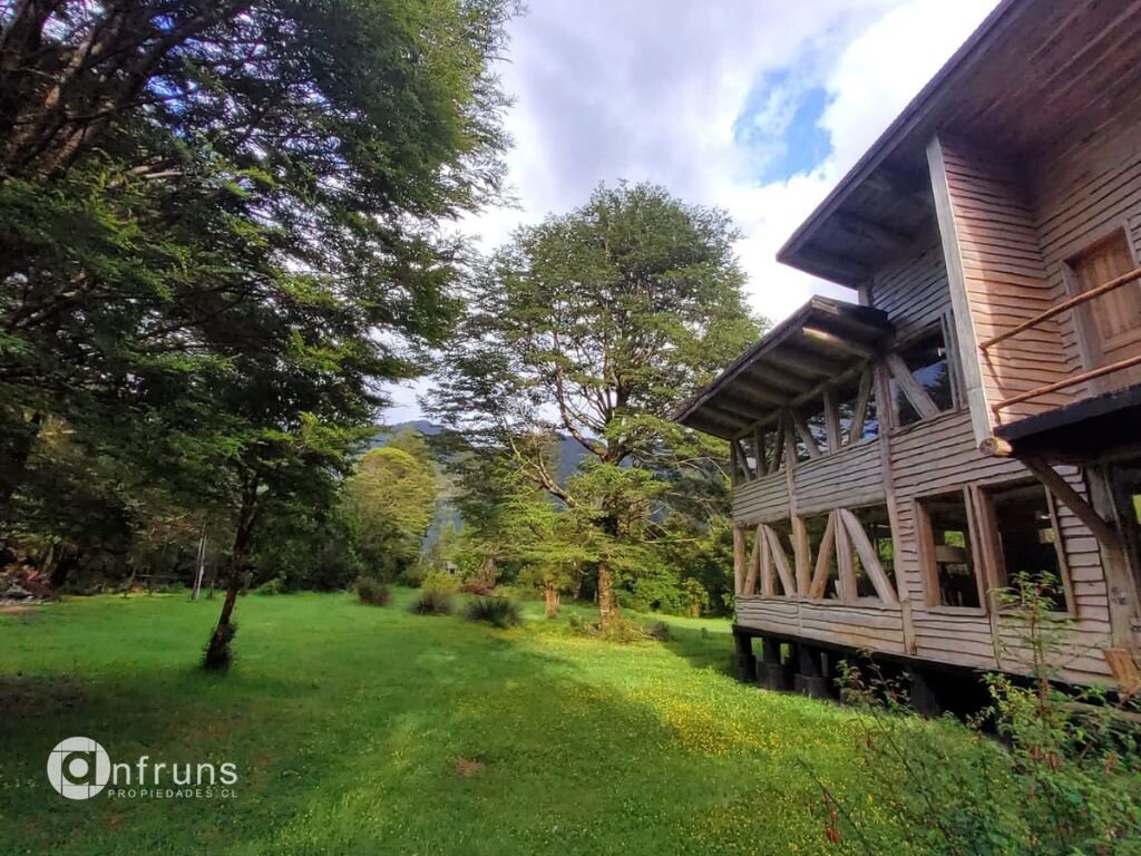 Forested area on the property with a wooden structure visible in the background, near Puerto Cisnes.